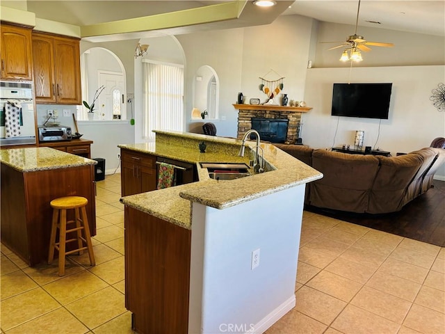 kitchen featuring lofted ceiling, a kitchen island with sink, white oven, sink, and ceiling fan