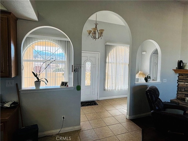 entryway with a stone fireplace, light tile patterned flooring, and a chandelier