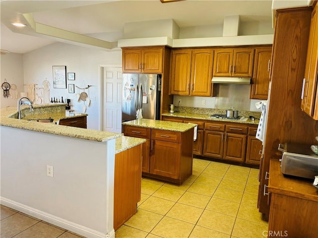 kitchen with light stone countertops, stainless steel appliances, sink, light tile patterned floors, and a center island with sink