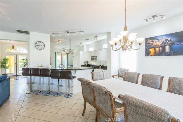 tiled dining space featuring a healthy amount of sunlight, sink, a chandelier, and french doors