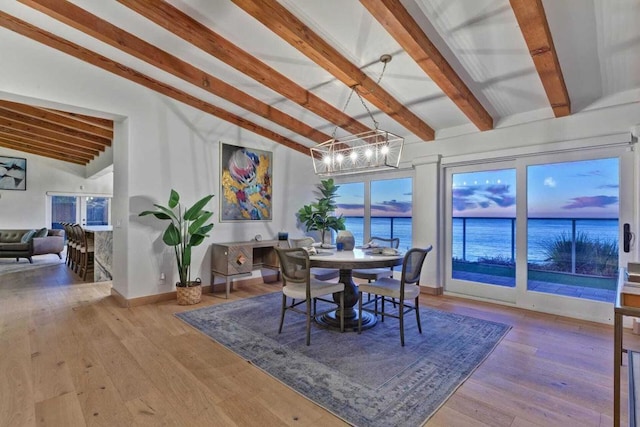 dining space with light wood-type flooring, lofted ceiling with beams, and a water view