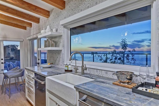 kitchen featuring light wood-type flooring, sink, a water view, beamed ceiling, and white cabinets