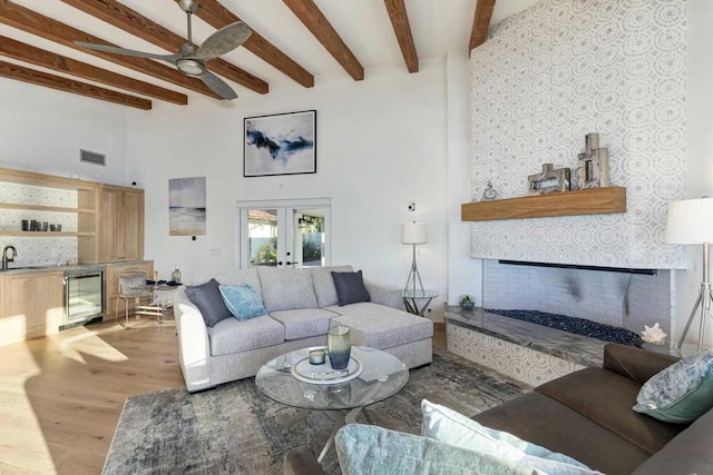 living room with beam ceiling, french doors, sink, beverage cooler, and light wood-type flooring