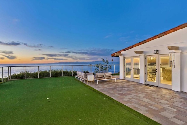 yard at dusk featuring outdoor lounge area, french doors, and a water view