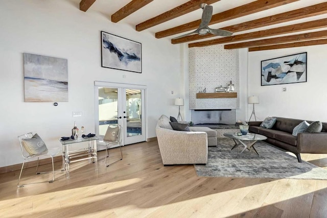 living room with ceiling fan, french doors, beamed ceiling, a fireplace, and light wood-type flooring