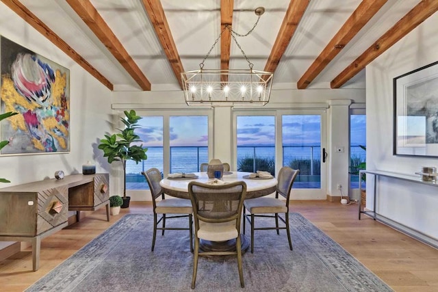 dining space featuring beam ceiling, a water view, an inviting chandelier, and wood-type flooring