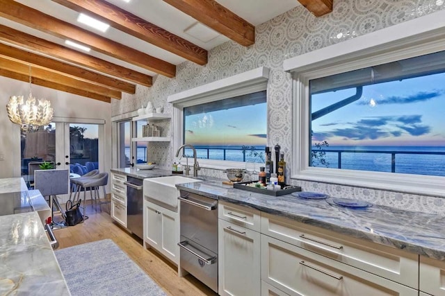 kitchen with white cabinetry, beamed ceiling, a water view, and light stone countertops