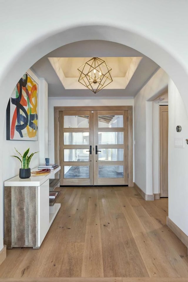 entryway with a raised ceiling, french doors, light hardwood / wood-style floors, and a notable chandelier