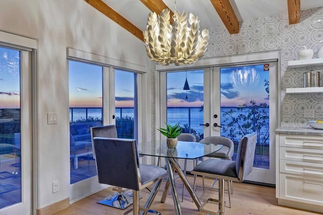 dining space with french doors, light hardwood / wood-style flooring, lofted ceiling with beams, a notable chandelier, and a water view