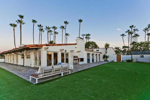 back house at dusk featuring outdoor lounge area, a yard, a patio, and a storage unit