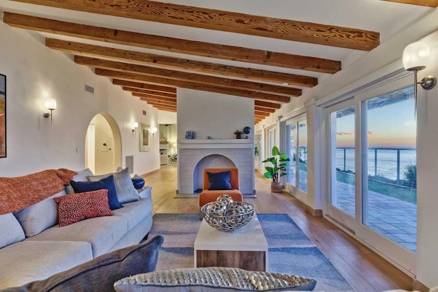 living room with beamed ceiling, a water view, and light hardwood / wood-style floors