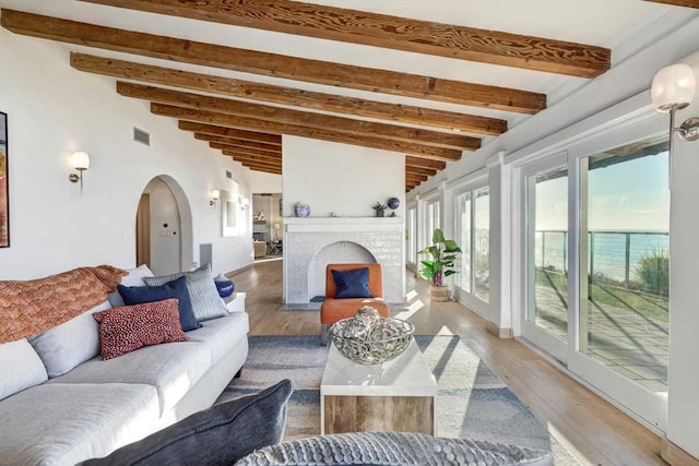 living room featuring a brick fireplace, lofted ceiling with beams, a water view, and light hardwood / wood-style flooring