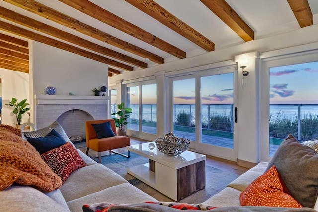 living room featuring beam ceiling, a fireplace, a water view, and hardwood / wood-style flooring