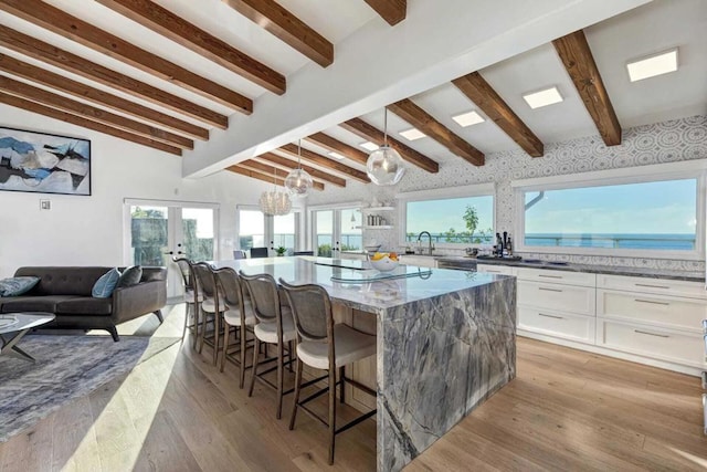 kitchen with french doors, pendant lighting, a water view, white cabinets, and a center island