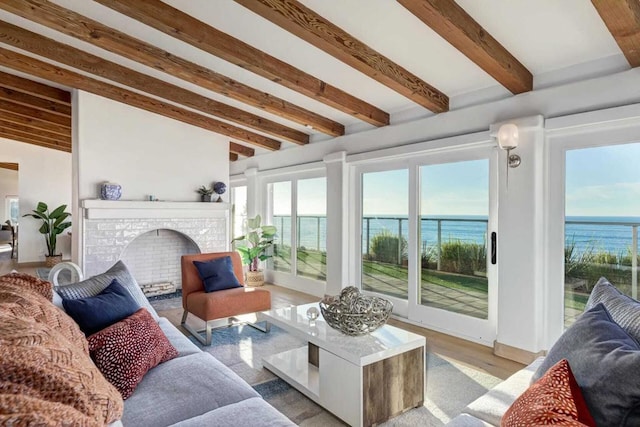 sunroom with beamed ceiling, a water view, and a brick fireplace