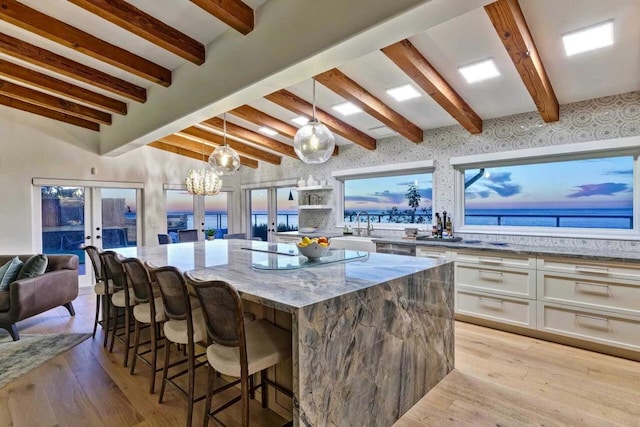 kitchen with light stone countertops, french doors, a water view, white cabinetry, and hanging light fixtures