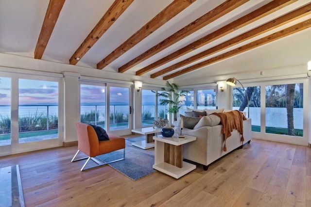 living room with vaulted ceiling with beams, a wealth of natural light, and light hardwood / wood-style flooring