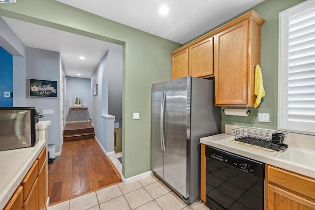 kitchen with stainless steel refrigerator, dishwasher, tile counters, and light hardwood / wood-style floors