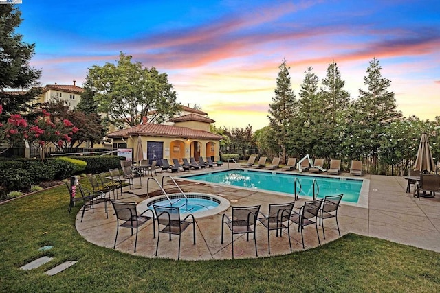 pool at dusk with a lawn, a patio, and a hot tub