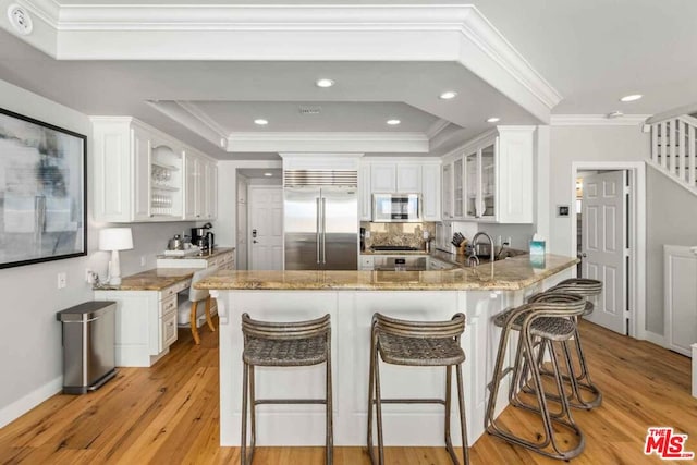 kitchen featuring white cabinets, a raised ceiling, kitchen peninsula, light hardwood / wood-style flooring, and stainless steel appliances