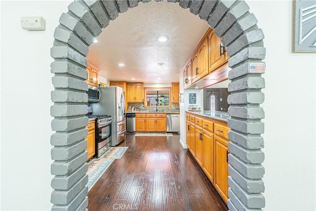 kitchen featuring sink, tasteful backsplash, dark hardwood / wood-style floors, a textured ceiling, and appliances with stainless steel finishes