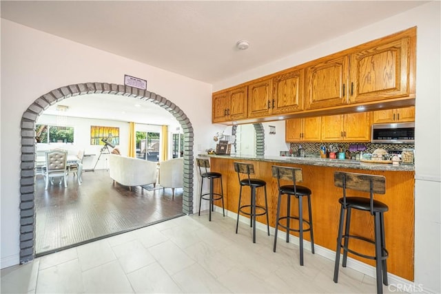 kitchen with a breakfast bar area, kitchen peninsula, tasteful backsplash, and light wood-type flooring