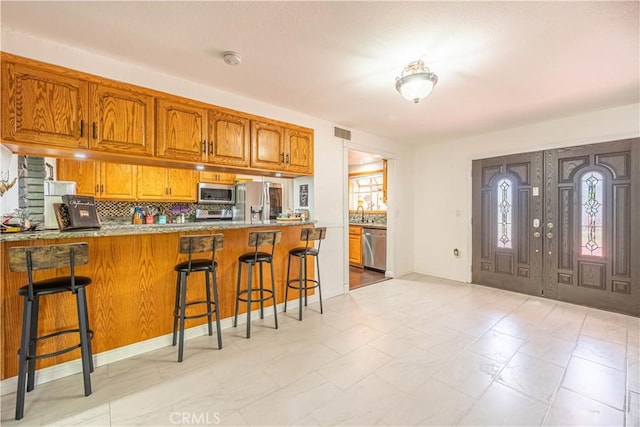 kitchen featuring a breakfast bar, kitchen peninsula, backsplash, and appliances with stainless steel finishes