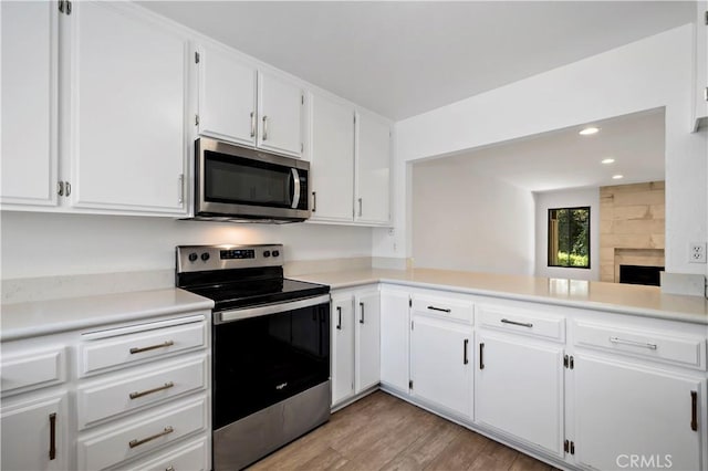 kitchen with kitchen peninsula, appliances with stainless steel finishes, a fireplace, white cabinets, and light wood-type flooring