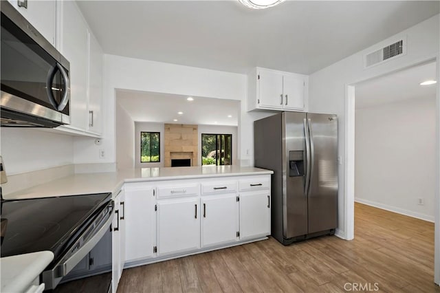 kitchen with kitchen peninsula, white cabinetry, stainless steel appliances, and light hardwood / wood-style flooring