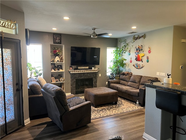 living room featuring ceiling fan, plenty of natural light, dark hardwood / wood-style flooring, and a tiled fireplace