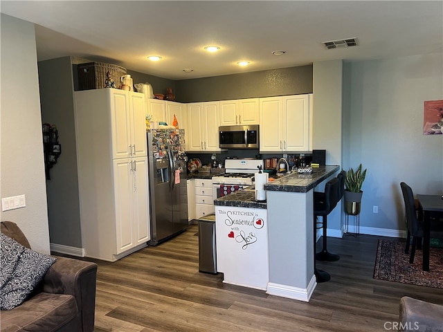 kitchen featuring white cabinets, kitchen peninsula, appliances with stainless steel finishes, a breakfast bar area, and dark hardwood / wood-style flooring