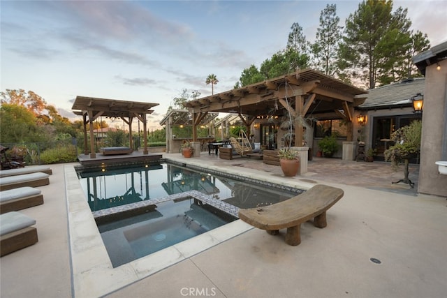 pool at dusk with an in ground hot tub and a patio area