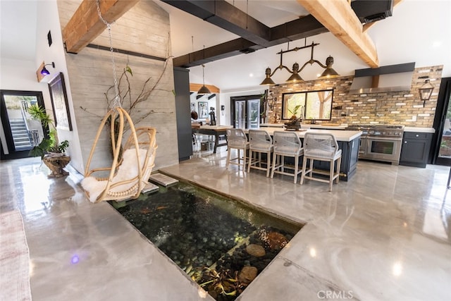 kitchen featuring range with two ovens, beamed ceiling, a high ceiling, decorative light fixtures, and a breakfast bar