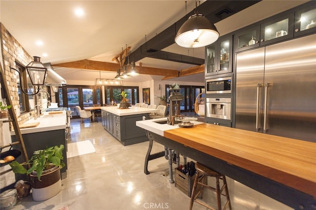 kitchen with built in appliances, beam ceiling, decorative light fixtures, and a kitchen island with sink