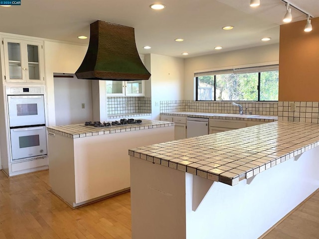 kitchen with tile counters, white cabinets, custom range hood, and white appliances