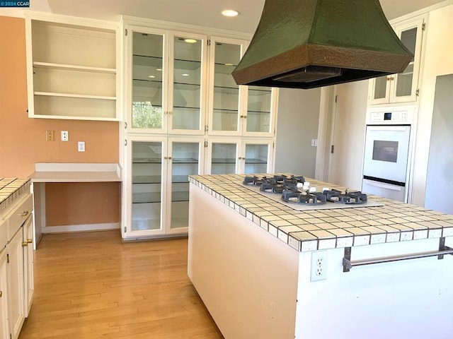 kitchen featuring custom range hood, white appliances, light hardwood / wood-style flooring, white cabinetry, and tile counters