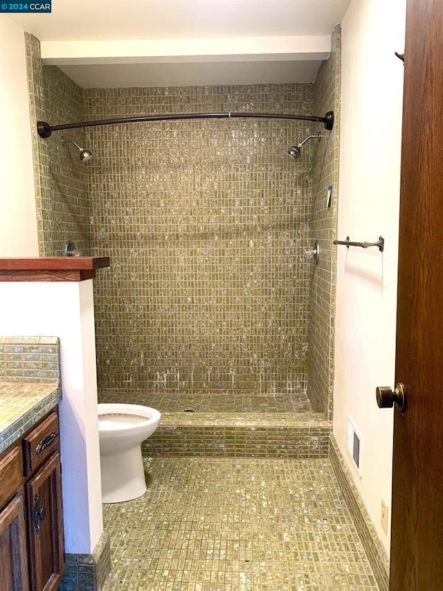 bathroom featuring a tile shower, vanity, and toilet