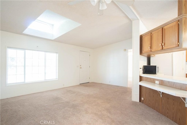 kitchen featuring ceiling fan, a skylight, and light carpet