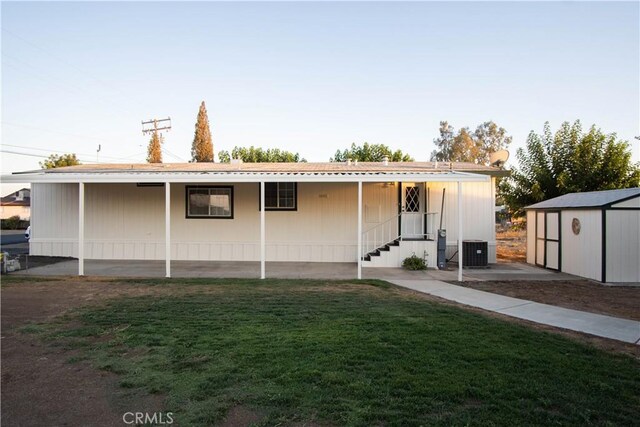 rear view of property with a lawn, cooling unit, and a storage shed