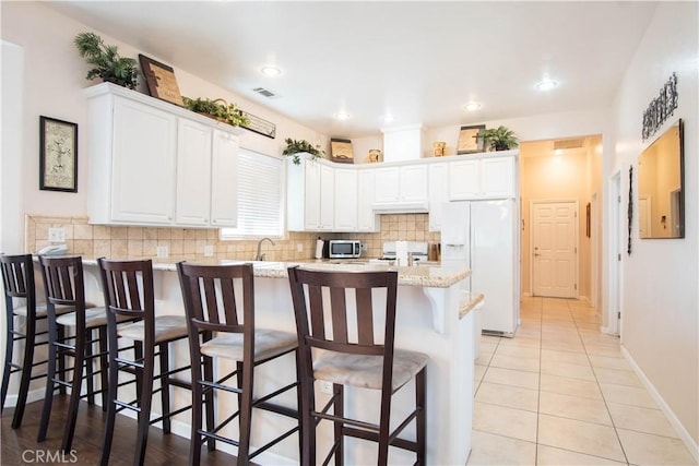 kitchen with white cabinetry, decorative backsplash, a breakfast bar area, and white fridge with ice dispenser