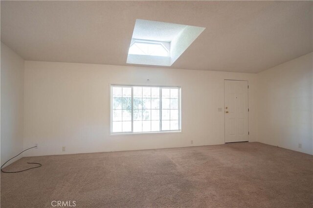 carpeted empty room featuring vaulted ceiling with skylight