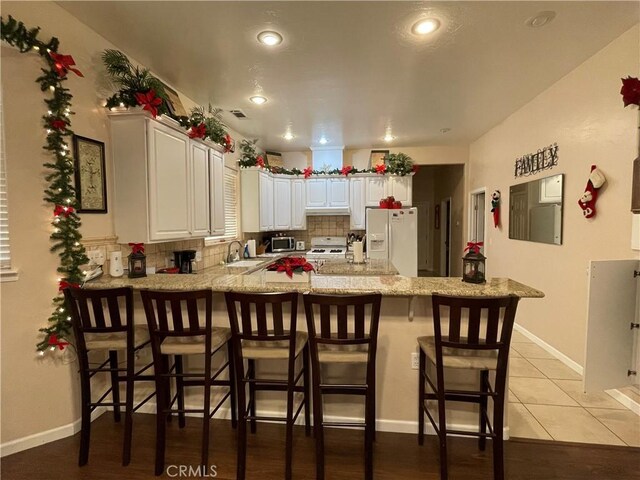 kitchen featuring white appliances, a kitchen breakfast bar, white cabinets, decorative backsplash, and kitchen peninsula