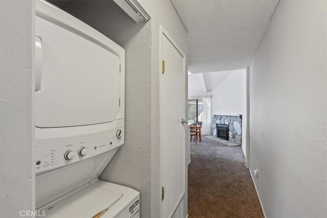 laundry area featuring stacked washer and clothes dryer, carpet, a textured ceiling, and a stone fireplace