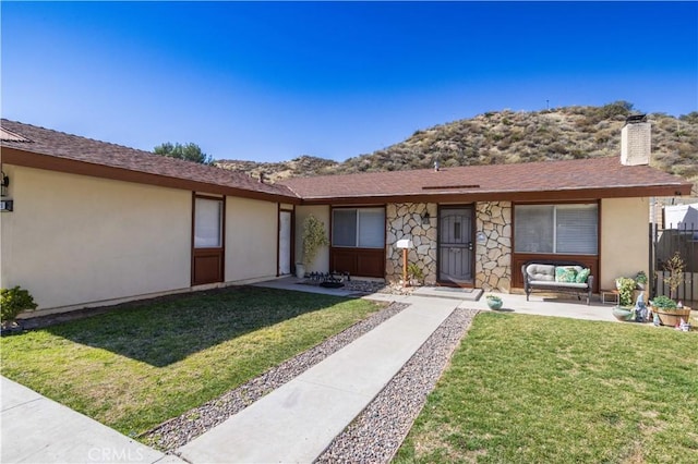 ranch-style home with a patio, a chimney, stucco siding, stone siding, and a front lawn