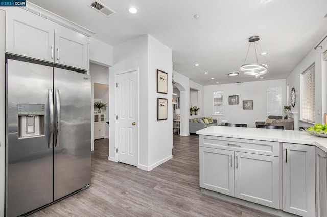 kitchen featuring white cabinets, stainless steel fridge, decorative light fixtures, and light hardwood / wood-style flooring