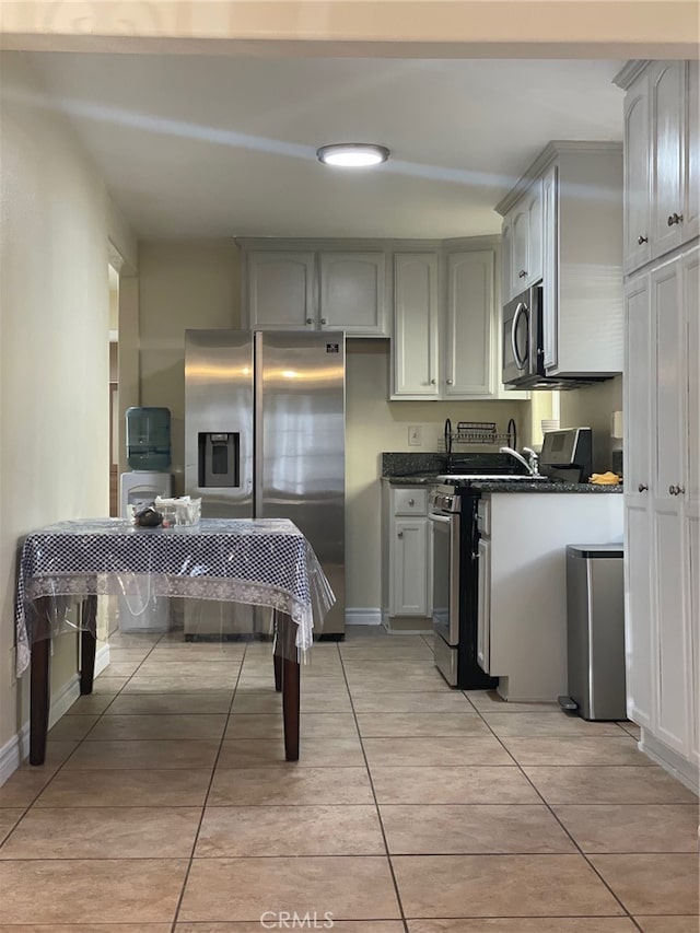 kitchen featuring gray cabinetry, stainless steel appliances, light tile patterned floors, and dark stone countertops