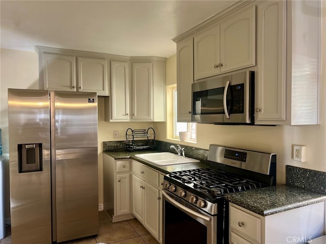 kitchen featuring appliances with stainless steel finishes, sink, cream cabinets, dark stone counters, and light tile patterned floors