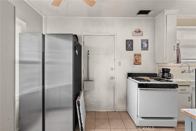 kitchen with backsplash, sink, white gas range oven, light tile patterned flooring, and white cabinetry