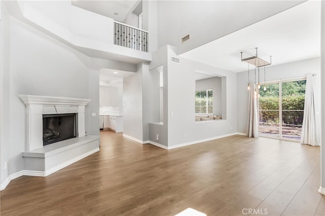 unfurnished living room with hardwood / wood-style flooring, a premium fireplace, and a high ceiling