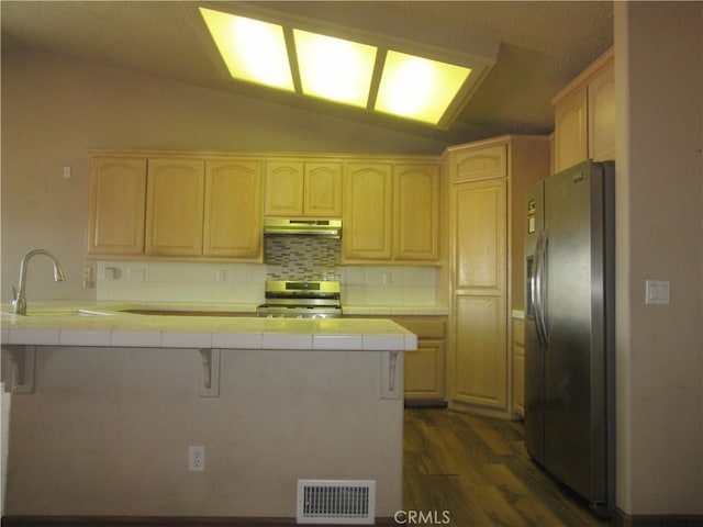 kitchen featuring appliances with stainless steel finishes, kitchen peninsula, vaulted ceiling, and tile countertops